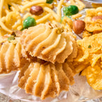 Close-up of piped Rasmalai Pistachio cookies topped with chopped pistachio, with namkeen behind