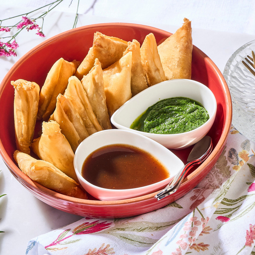 Halal Potato Samosas in a red bowl with green coriander chutney and tamarind dipping sauce