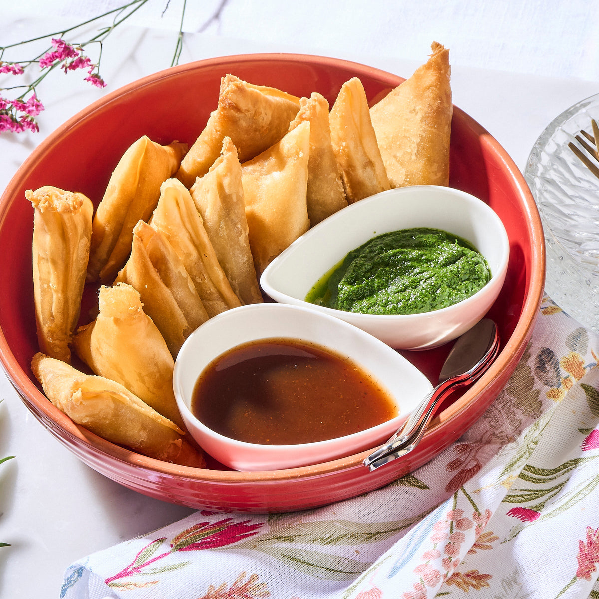 Halal Potato Samosas in a red bowl with green coriander chutney and tamarind dipping sauce