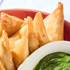 Close-up of golden, crisp Potato Samosas beside a bowl of green coriander chutney