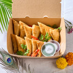 Potato Samosas in an open takeaway box with chilli, coriander and a pot of green chutney
