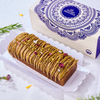 Eggless Pistachio Cardamom Voyage Cake topped with pistachio praline, rose petals and silver leaf by its gift box