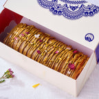 Pistachio Cardamom Voyage Cake in an open blue-patterned gift box showing a halal logo and praline drizzle