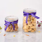 Two glass jars of eggless Rasmalai Pistachio Cookies with clip lids, tied with purple ribbon