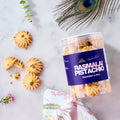 Halal Rasmalai Pistachio Cookies in a jar labelled Fragrant & Rich, with piped cookies scattered on marble
